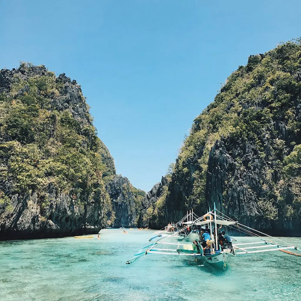 A small boat floating in the turquoise waters of Bacuit Bay, surrounded by limestone cliffs.