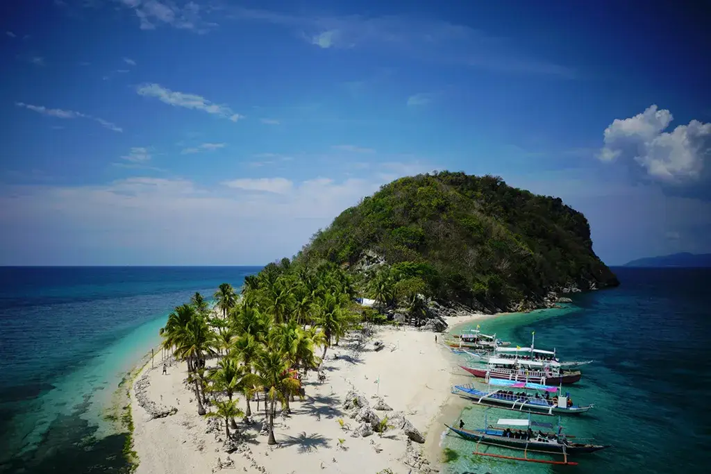 Aerial view of Gigantes Island Philippines with white sand beach, palm trees, turquoise water, and colorful outrigger boats along the shoreline.