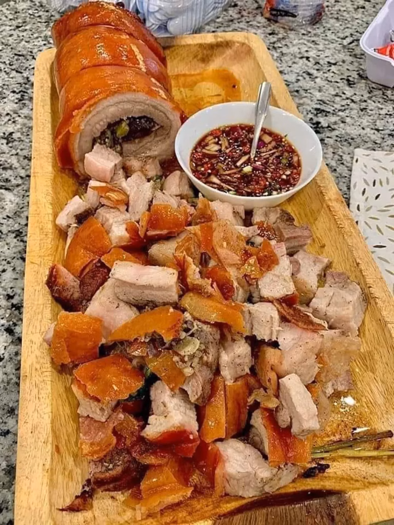Sliced Cebu lechon on a wooden cutting board showing crispy golden crackling skin, juicy herb-stuffed pork meat, and a bowl of spiced vinegar dipping sauce, a signature dish of the Sinulog Festival food experience in Cebu, Philippines.