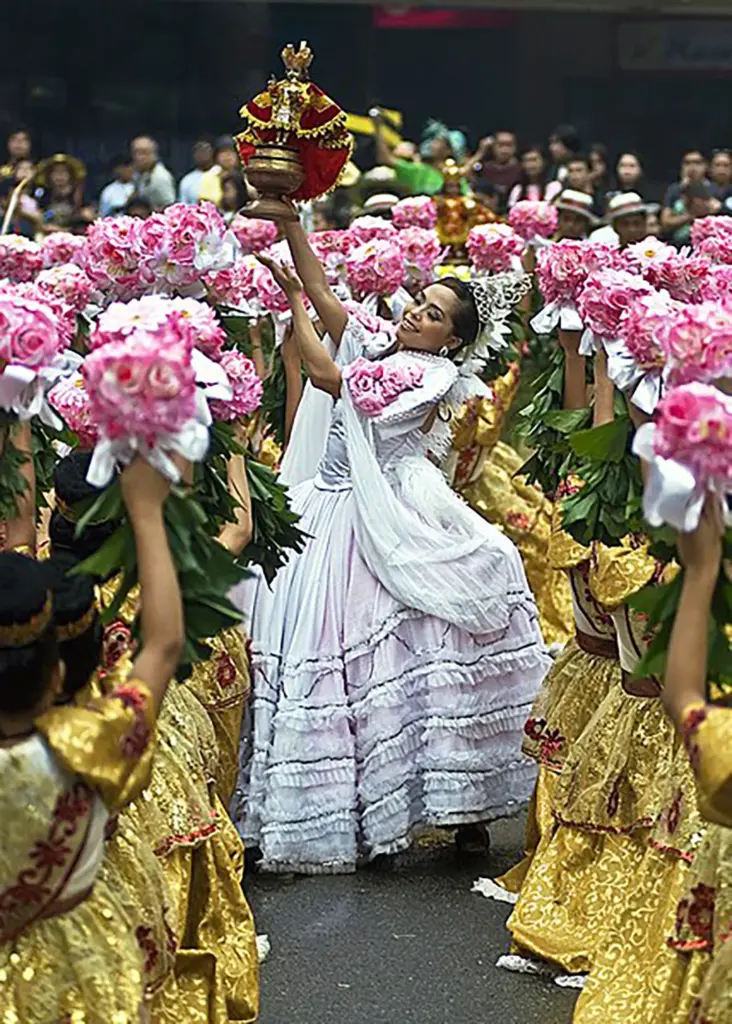 A picture from the Sinulog Festival of a woman dancing, adorned in costume, with a religious statue in her hands.