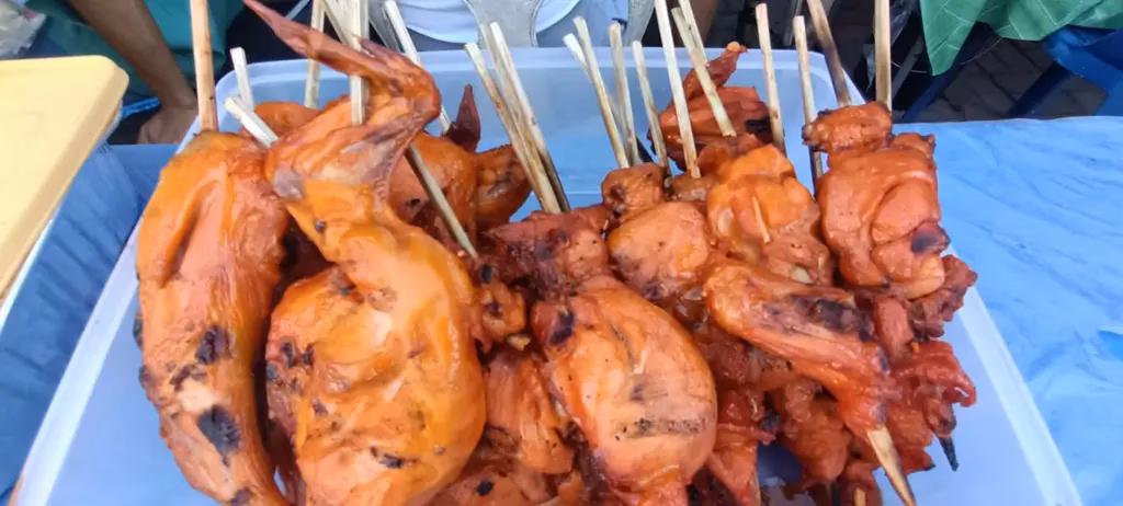 A tray of grilled chicken inasal on bamboo skewers at a Sinulog Festival street food stall in Cebu City, Philippines, showing golden charred chicken wings and thighs marinated in the signature annatto and vinegar blend of this classic Filipino dish.